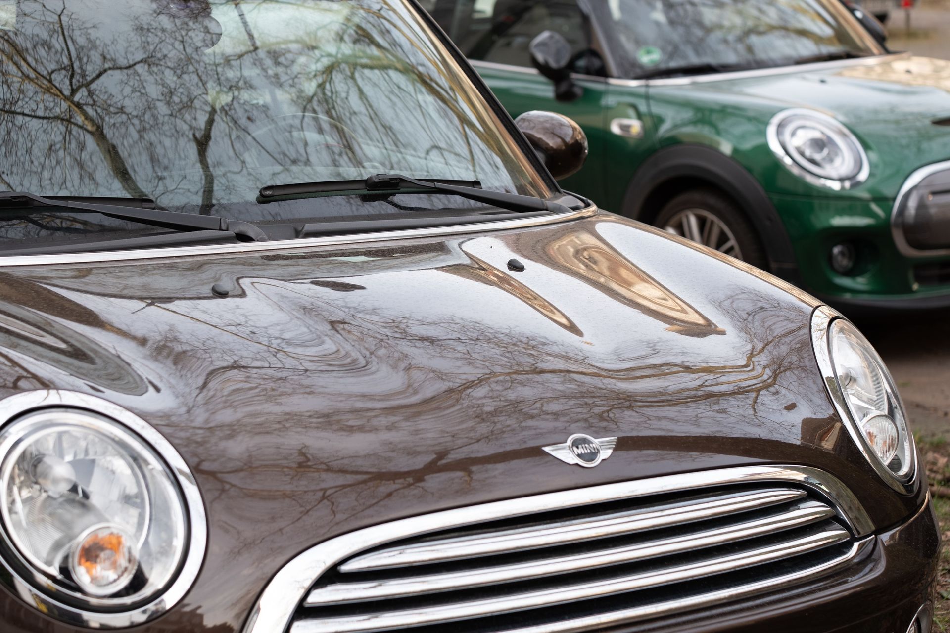 Close-up of two Mini Cooper cars reflecting urban surroundings, emphasizing modern design.