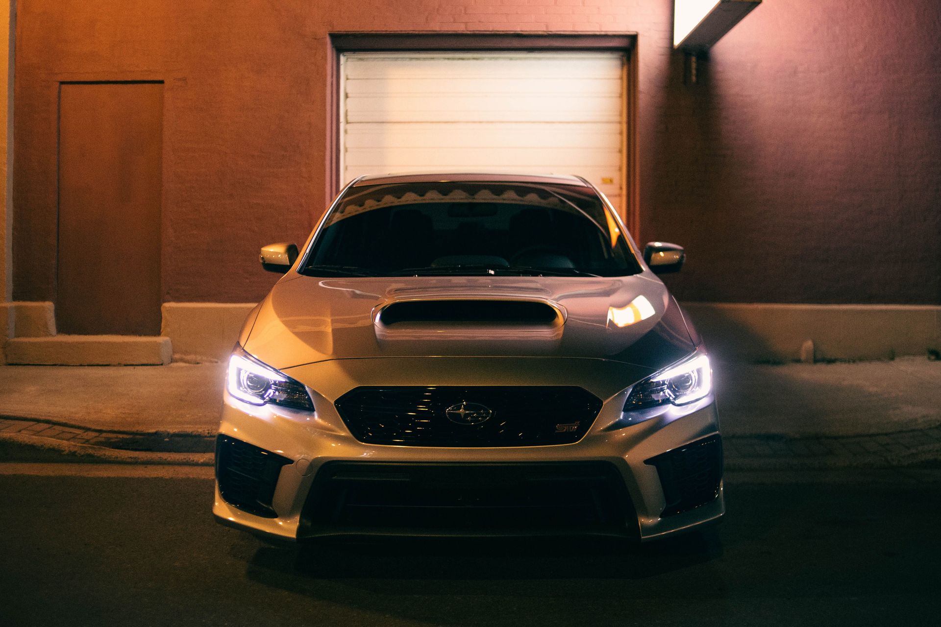 A front-facing sedan car with headlights on, captured at night in an urban setting.